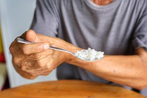 Elderly man holding his hand while eating due to hand tremor