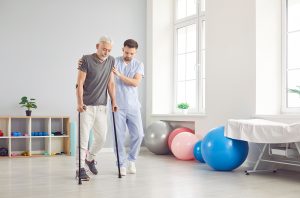 Person with ALS using forearm crutches and being helped by a caregiver